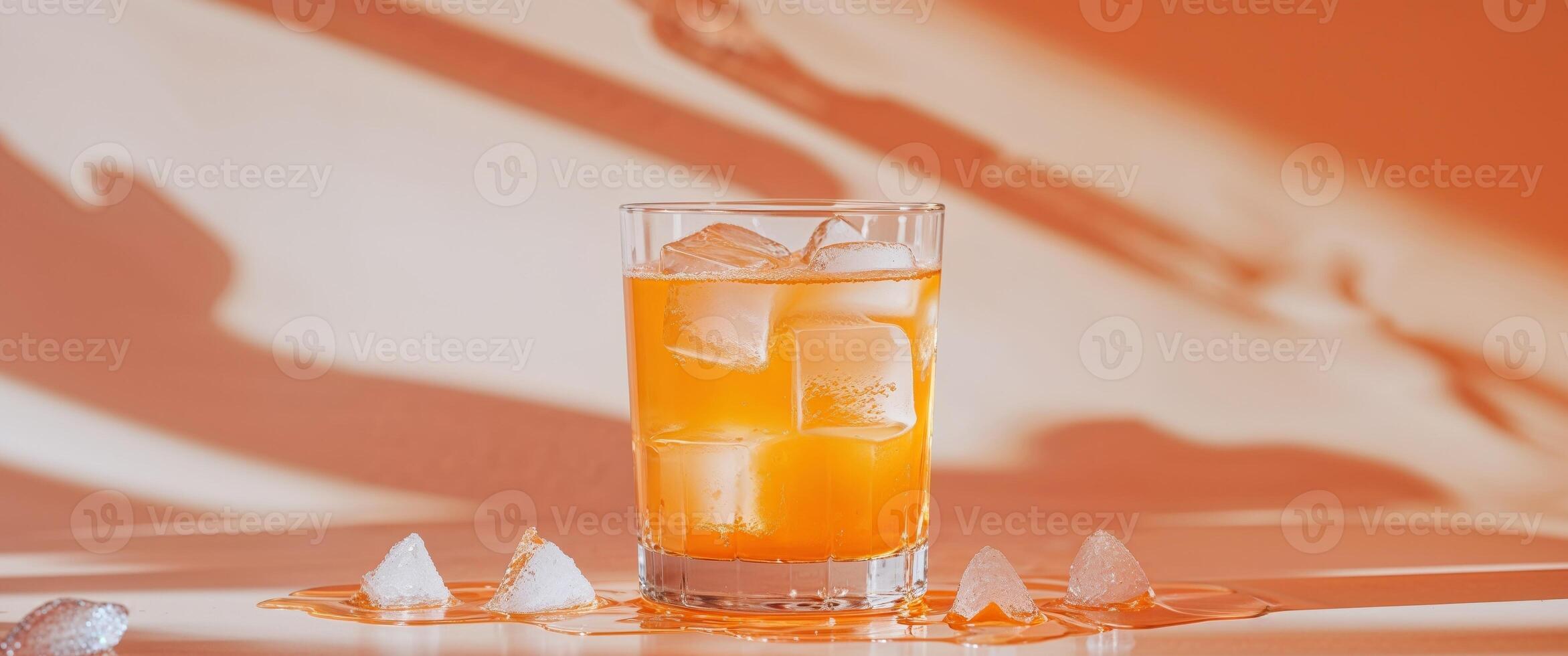 Refreshing Orange Drink with Ice in a Clear Glass on Orange Background. photo