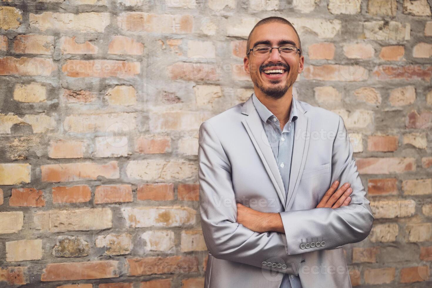 Adilt man in suit is standing in the front of brick wall, looking at camera and smiling. photo
