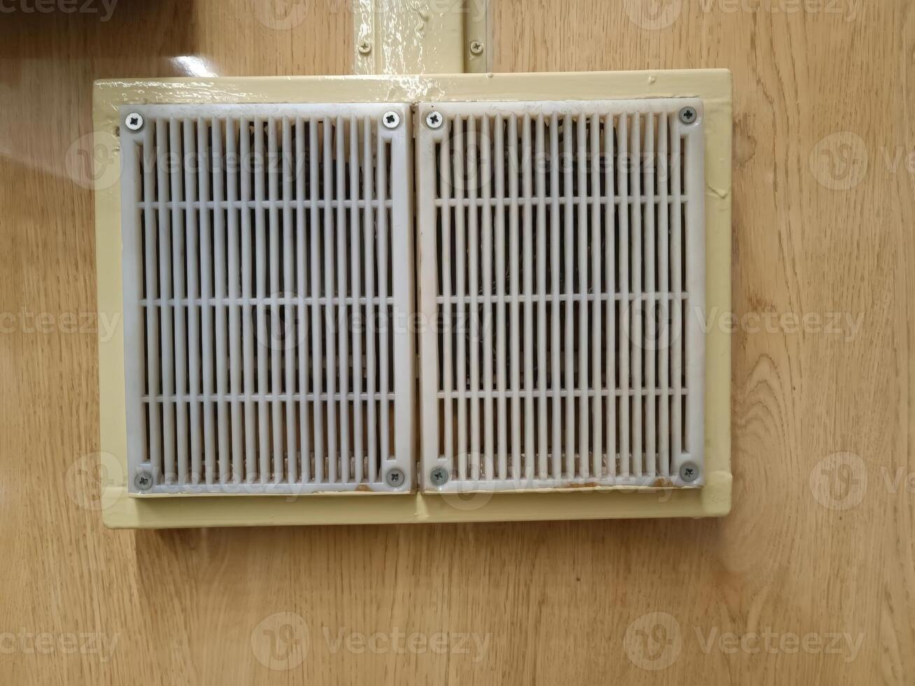 A wall-mounted air vent with a beige frame and a white grille, providing ventilation in a building. photo