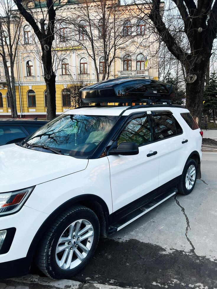 Lviv, Ukraine - February 12, 2025- White Ford Explorer SUV vehicle with Thule rooftop cargo box parked near historic building in city photo