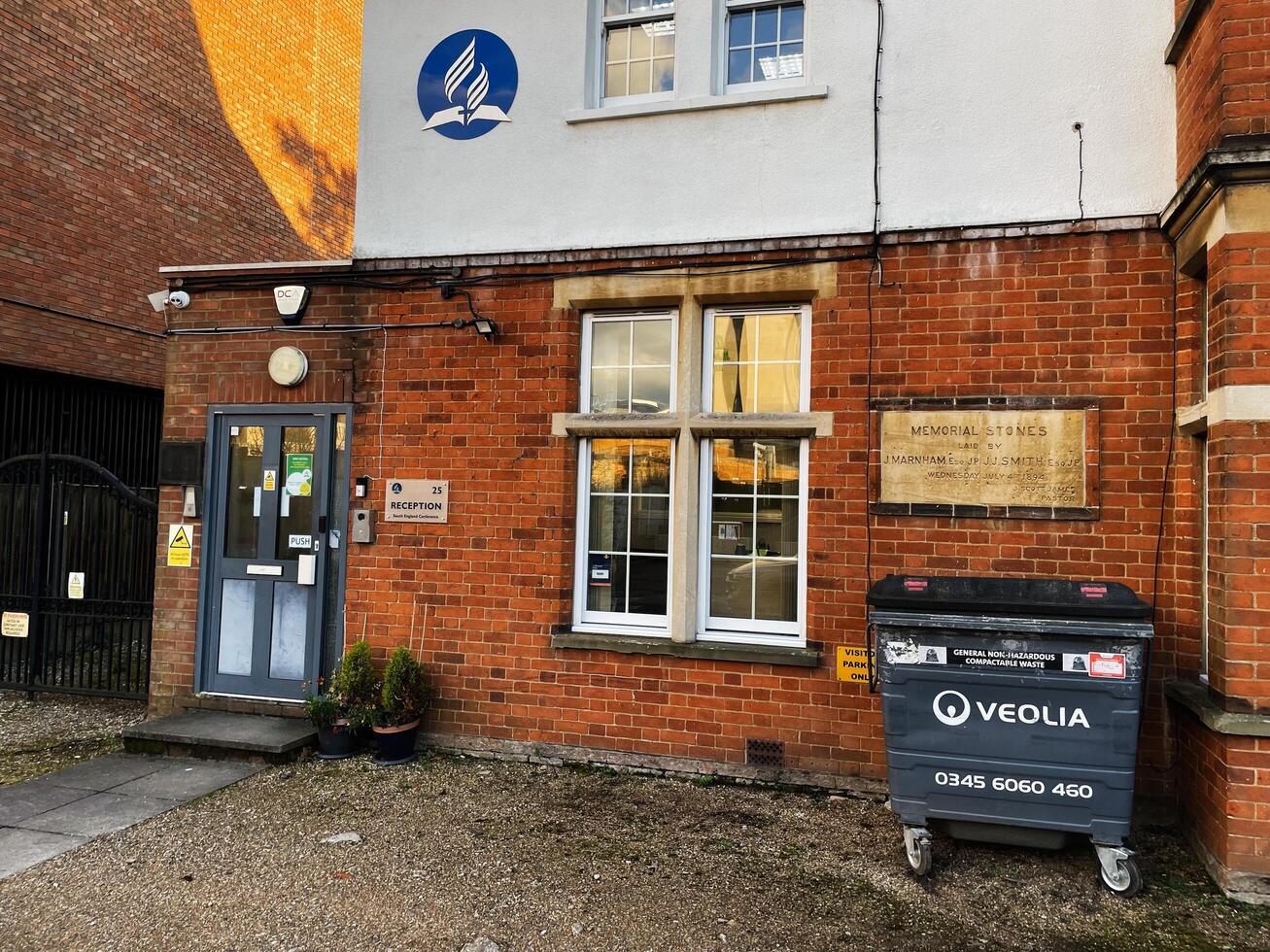 London, UK - March 02, 2025- Red brick building with a front door, signage, and waste bin outside photo