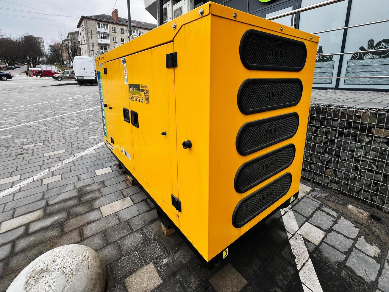 Kyiv, Ukraine - March 04, 2025- Yellow Industrial Aksa Generator Standing Outdoors on a Paved Urban Area photo