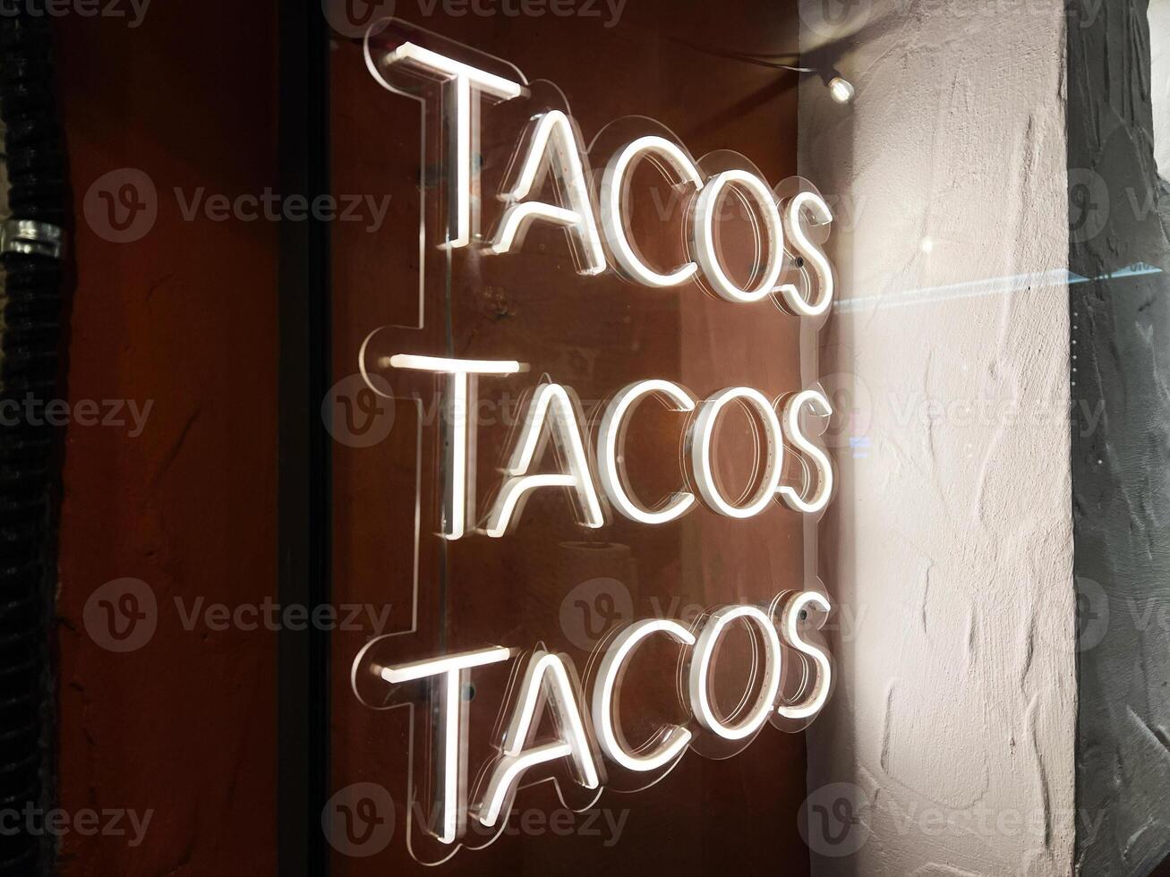 Illuminated neon tacos sign with a vibrant design on a textured wall photo