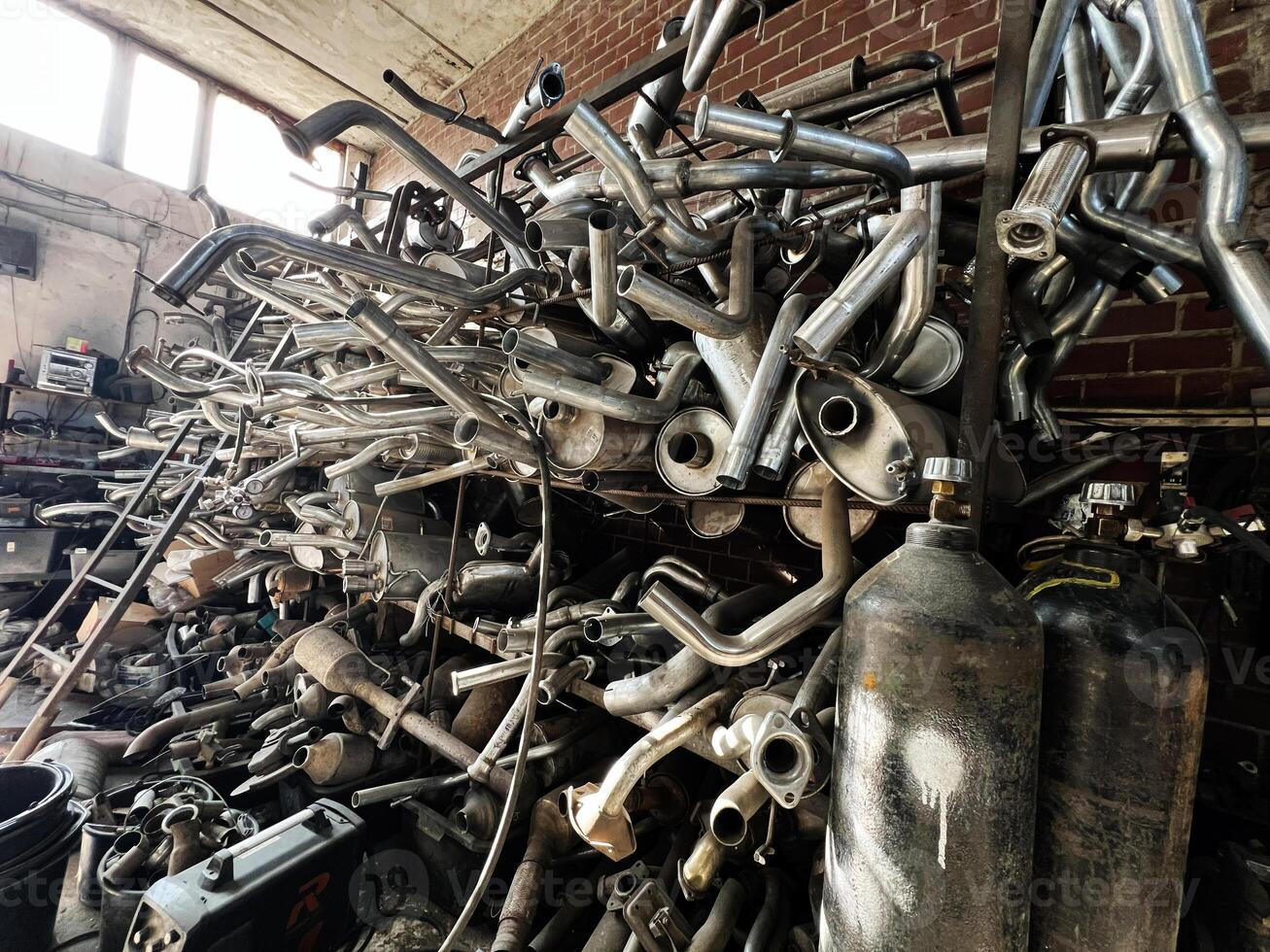 A heap of metal exhaust pipes and canisters in a rustic workshop setting photo