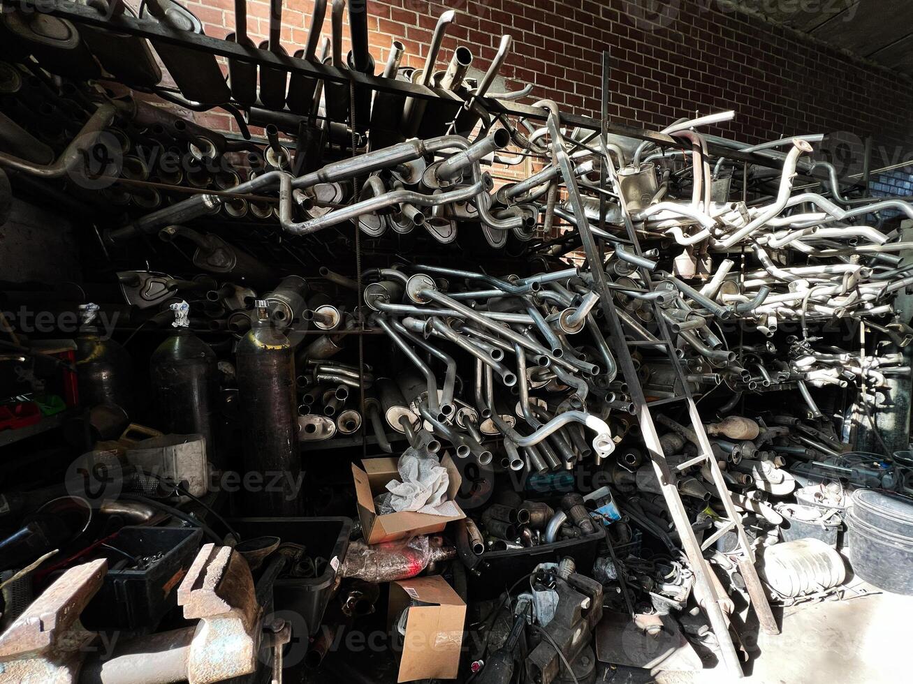 Stacked metal exhaust pipes and machinery inside a cluttered industrial workshop photo