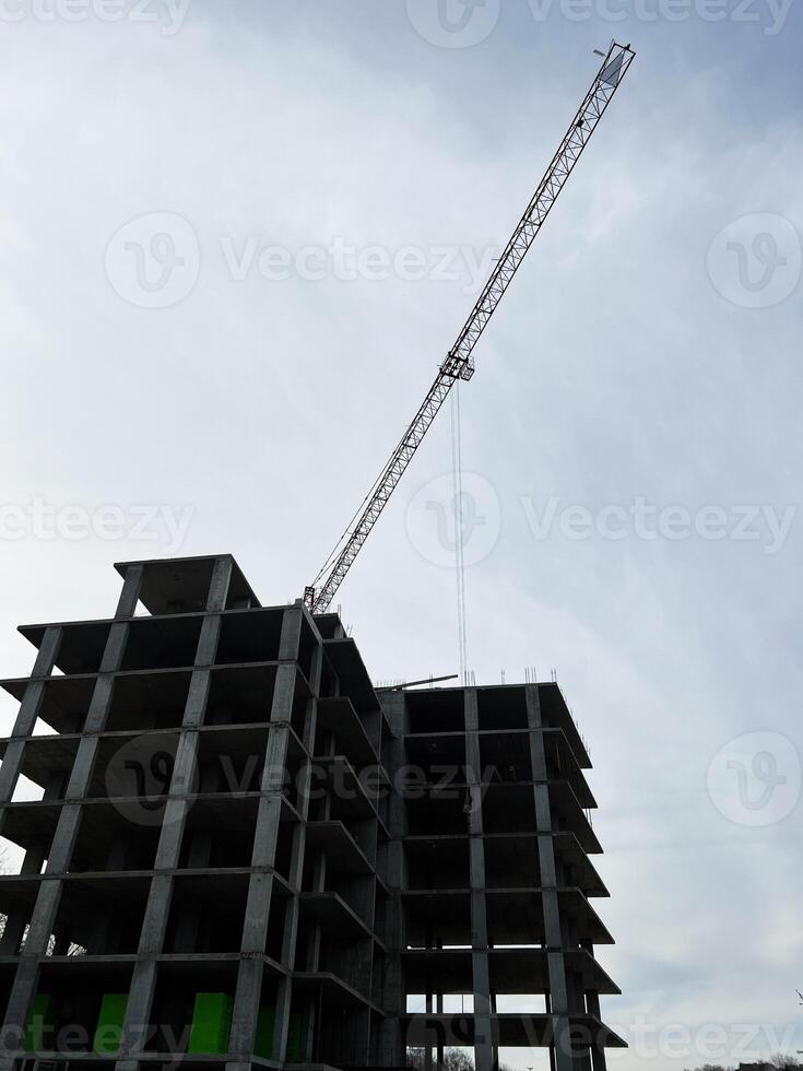 Tall construction crane beside an unfinished building under a bright cloudy sky photo