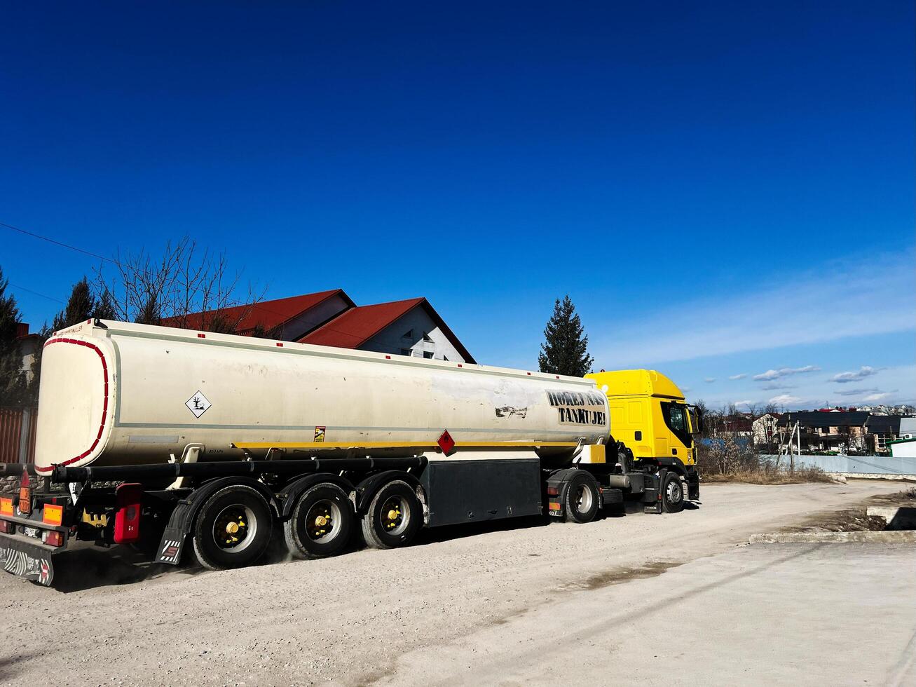 Kyiv, Ukraine - March 10, 2025- Yellow fuel tanker truck parked near houses under a clear blue sky photo