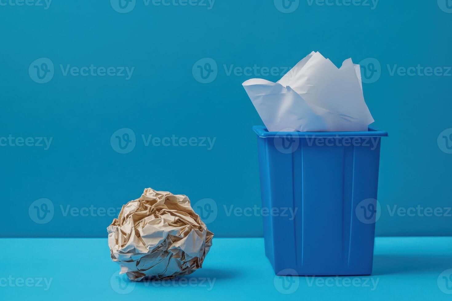 A blue trash can sits next to a pile of paper photo