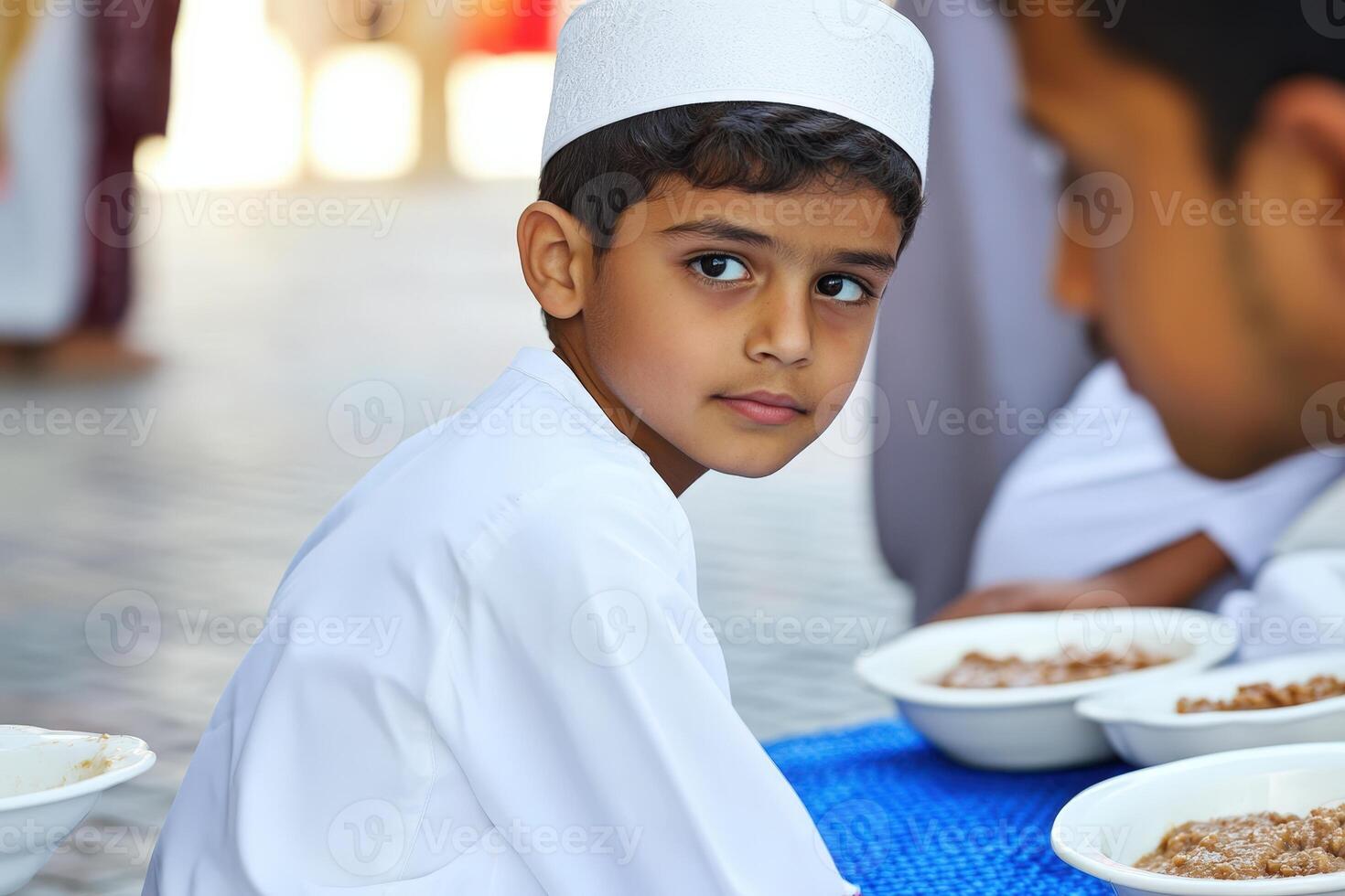 A young boy in a white shirt sitting at a table with food photo