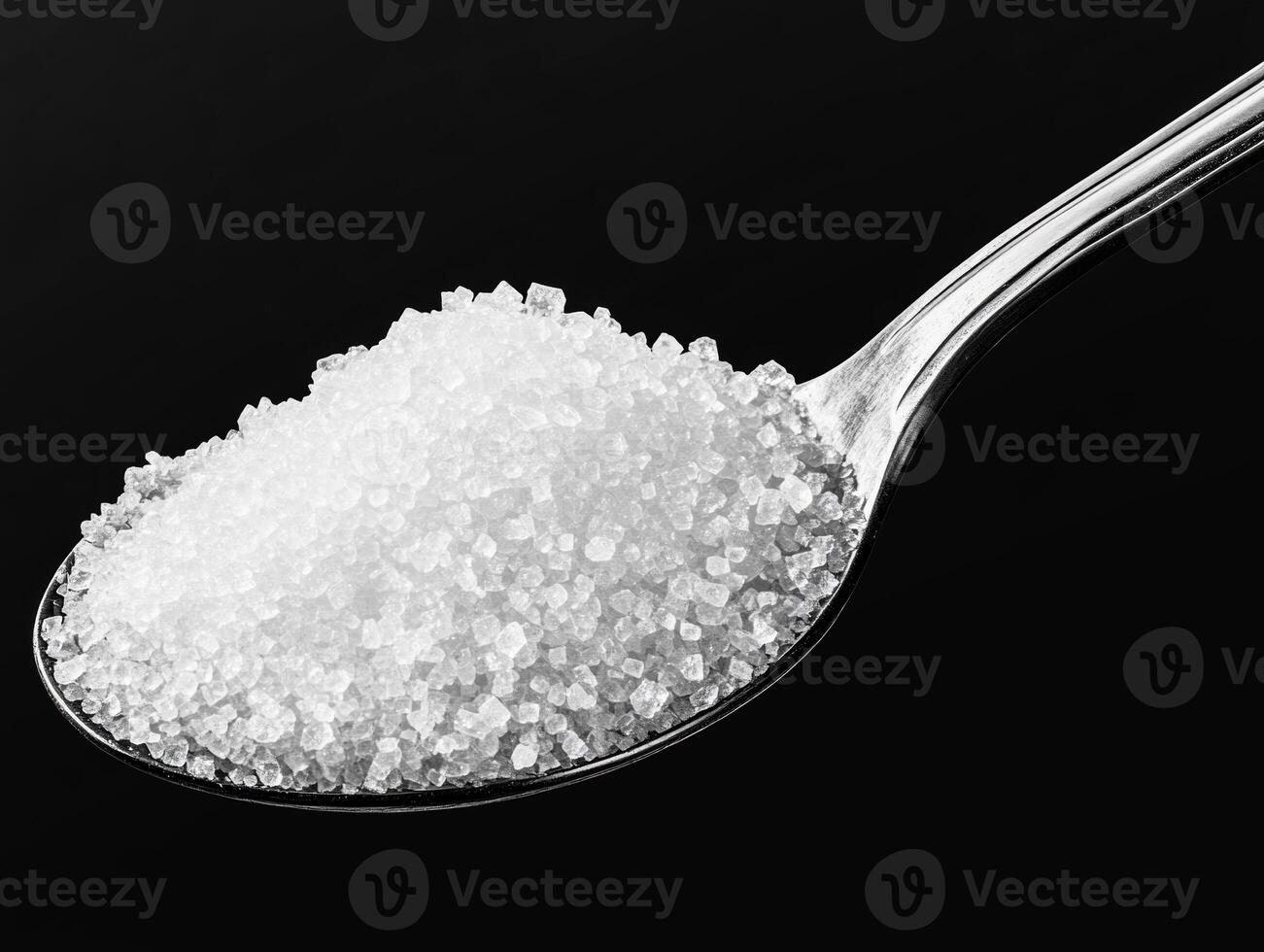 Close-up view of granulated sugar on a spoon against black background photo