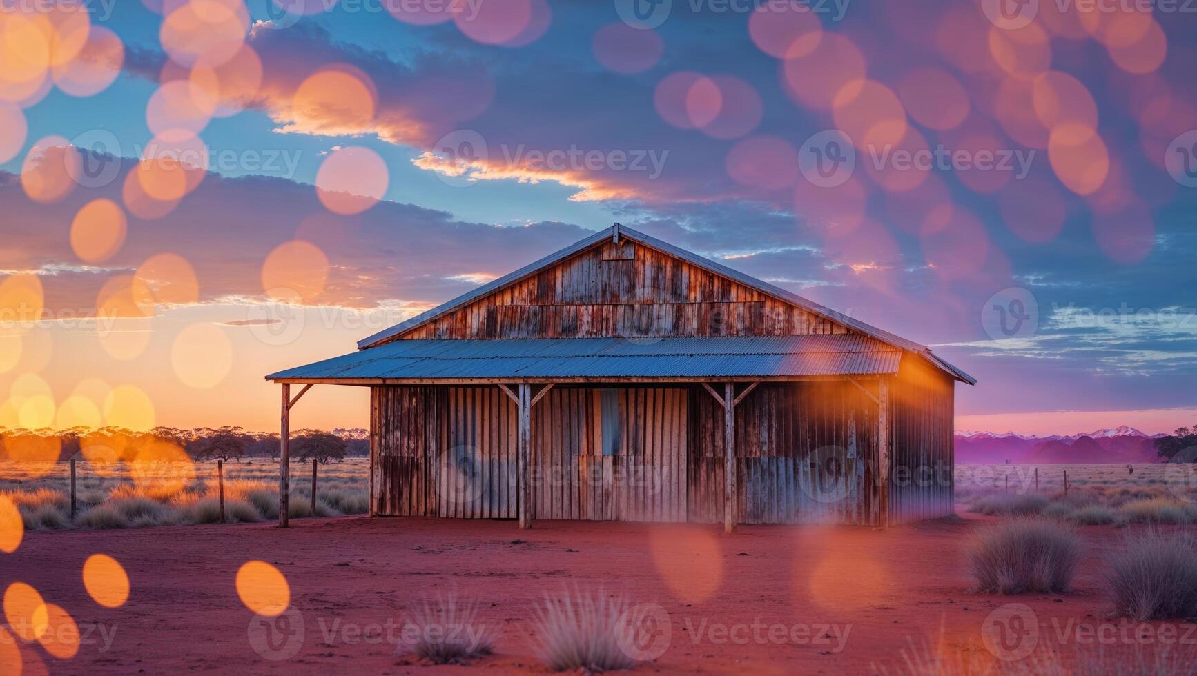 Weathered barn stands alone under a colorful sunset in a vast desert landscape with soft bokeh lights photo
