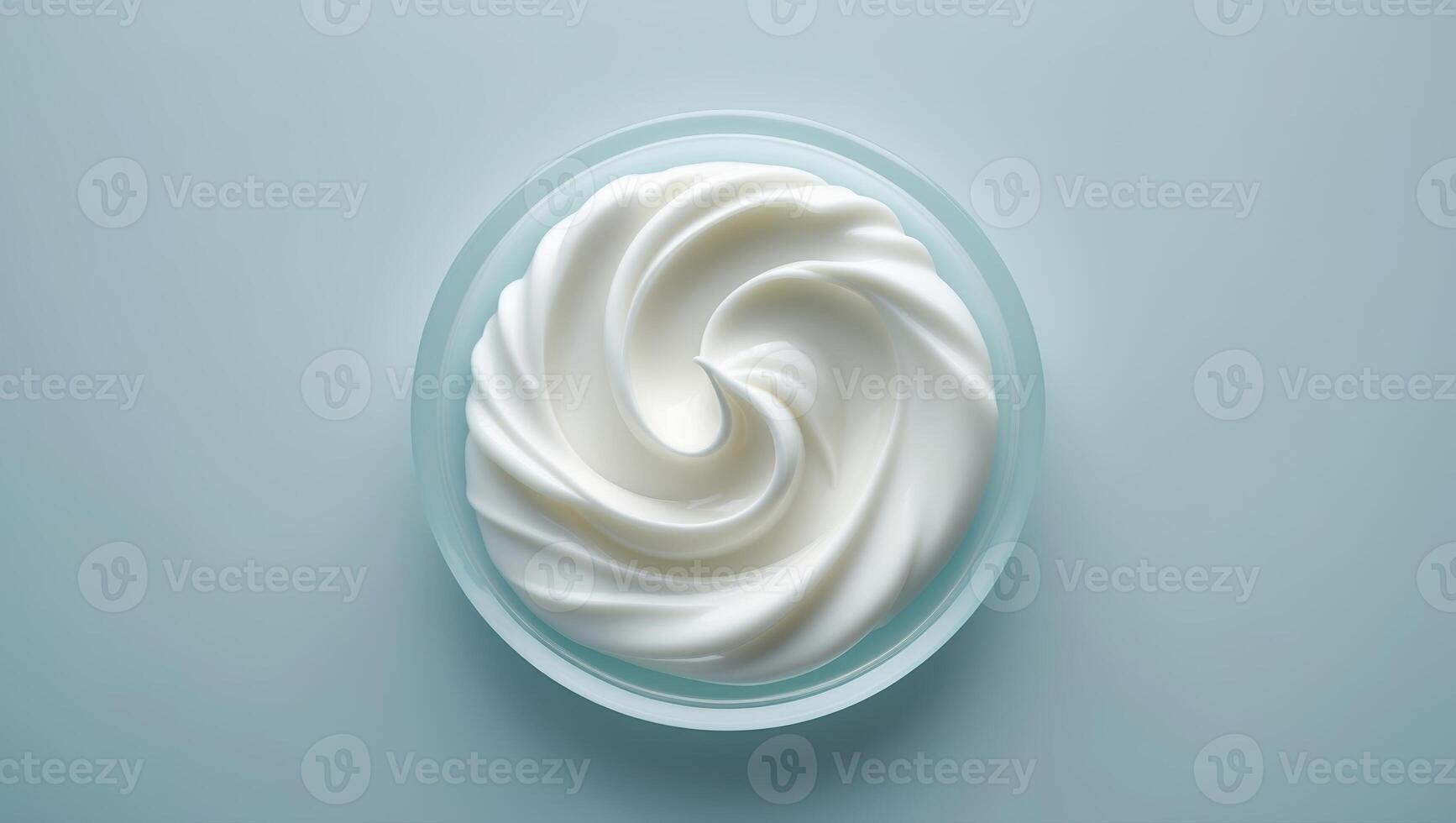 Whipped cream swirls in a clear bowl on a light blue background, showcasing a delicious dessert topping photo
