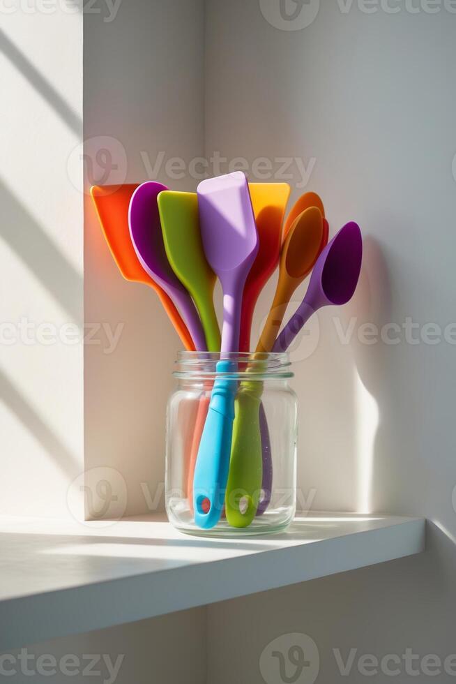 Colorful silicone spatulas arranged in a jar on a kitchen shelf with sunlight casting shadows photo