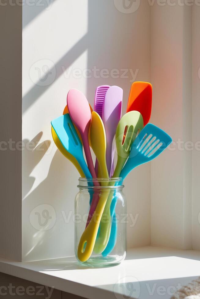 Colorful silicone kitchen utensils in a jar illuminated by sunlight on a windowsill photo