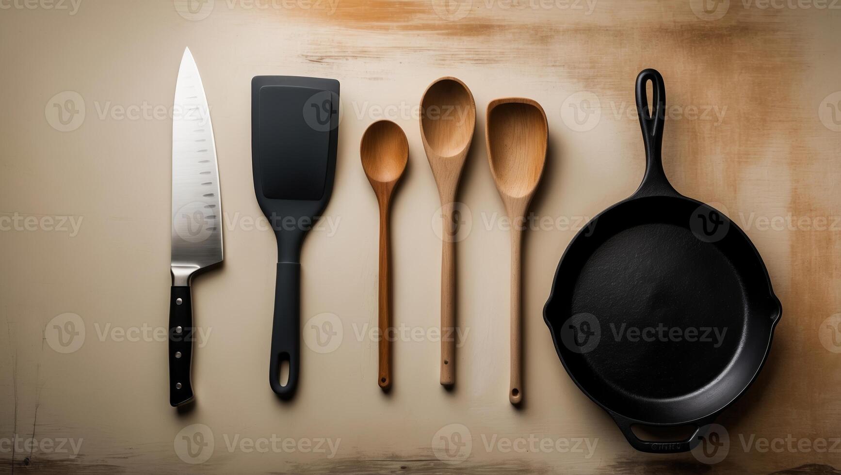 Kitchen utensils displayed on a wooden surface featuring a knife, spatula, wooden spoons, and cast iron skillet photo