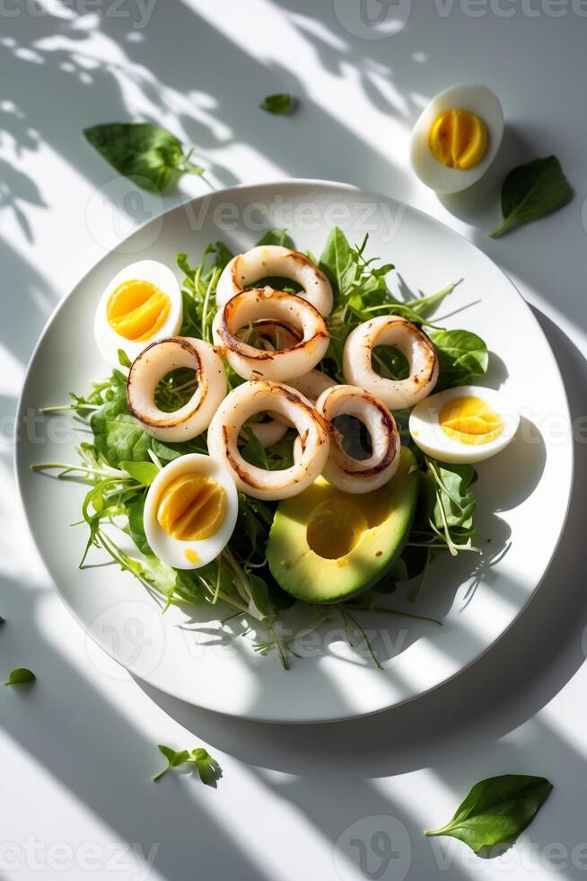 Fresh salad with grilled squid, avocado, and sliced hard-boiled eggs on a white plate under natural light photo