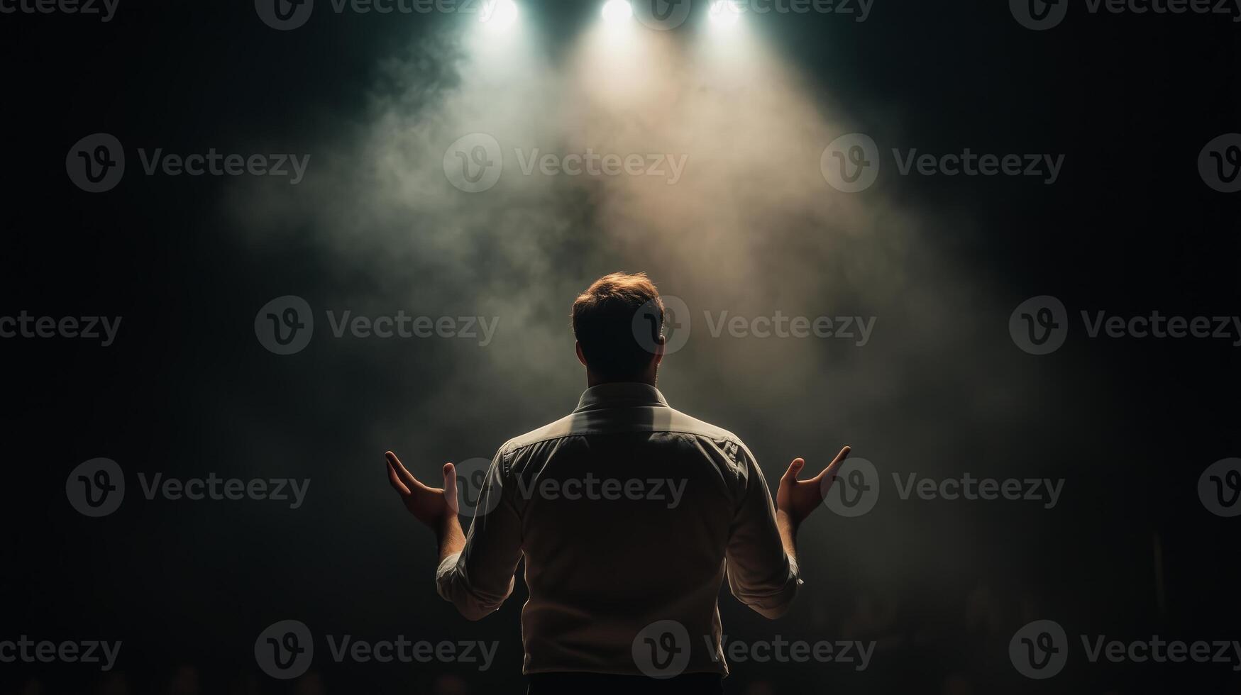 Person standing on stage with raised arms under spotlight in a smoky environment, conveying emotion and engagement photo