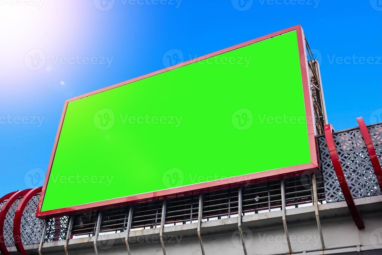 Blank green screen billboard on a building structure with a clear blue sky background, ideal for advertising mockups. photo