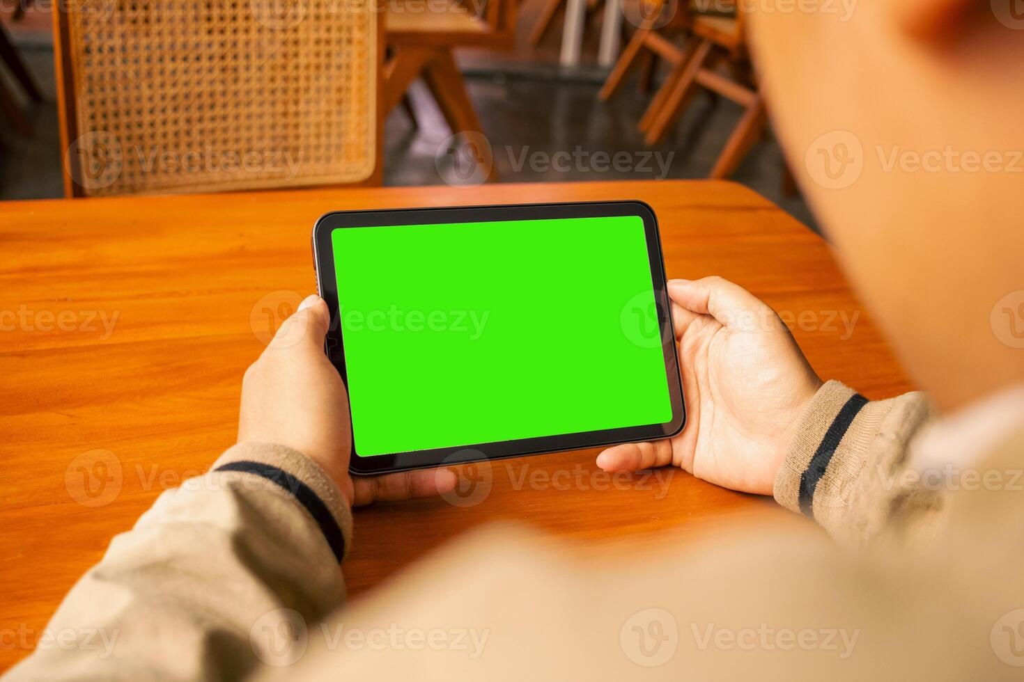 Man viewing a tablet with a blank green screen in a cozy cafe setting, perfect for design templates. photo