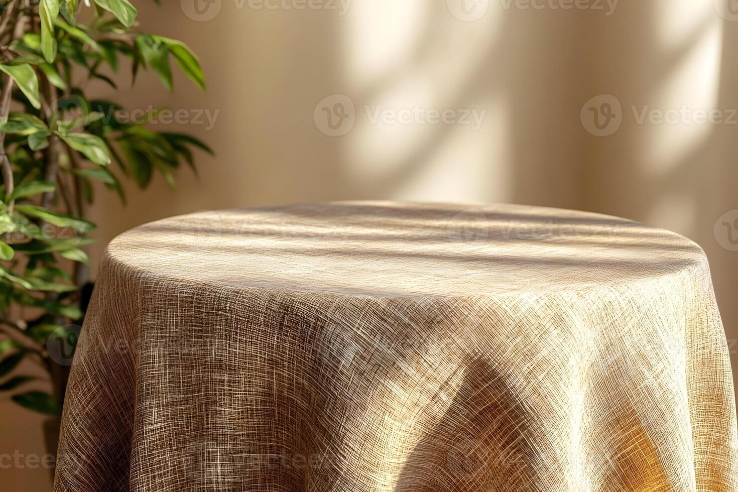 Empty round table draped with beige linen tablecloth, sunlight and plant. photo