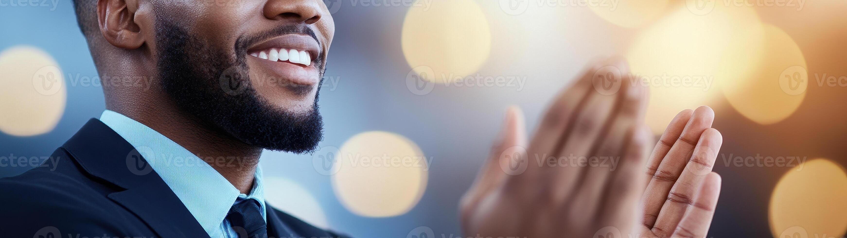Smiling man in suit clapping hands, expressing joy and appreciation in professional setting with blurred lights in background photo