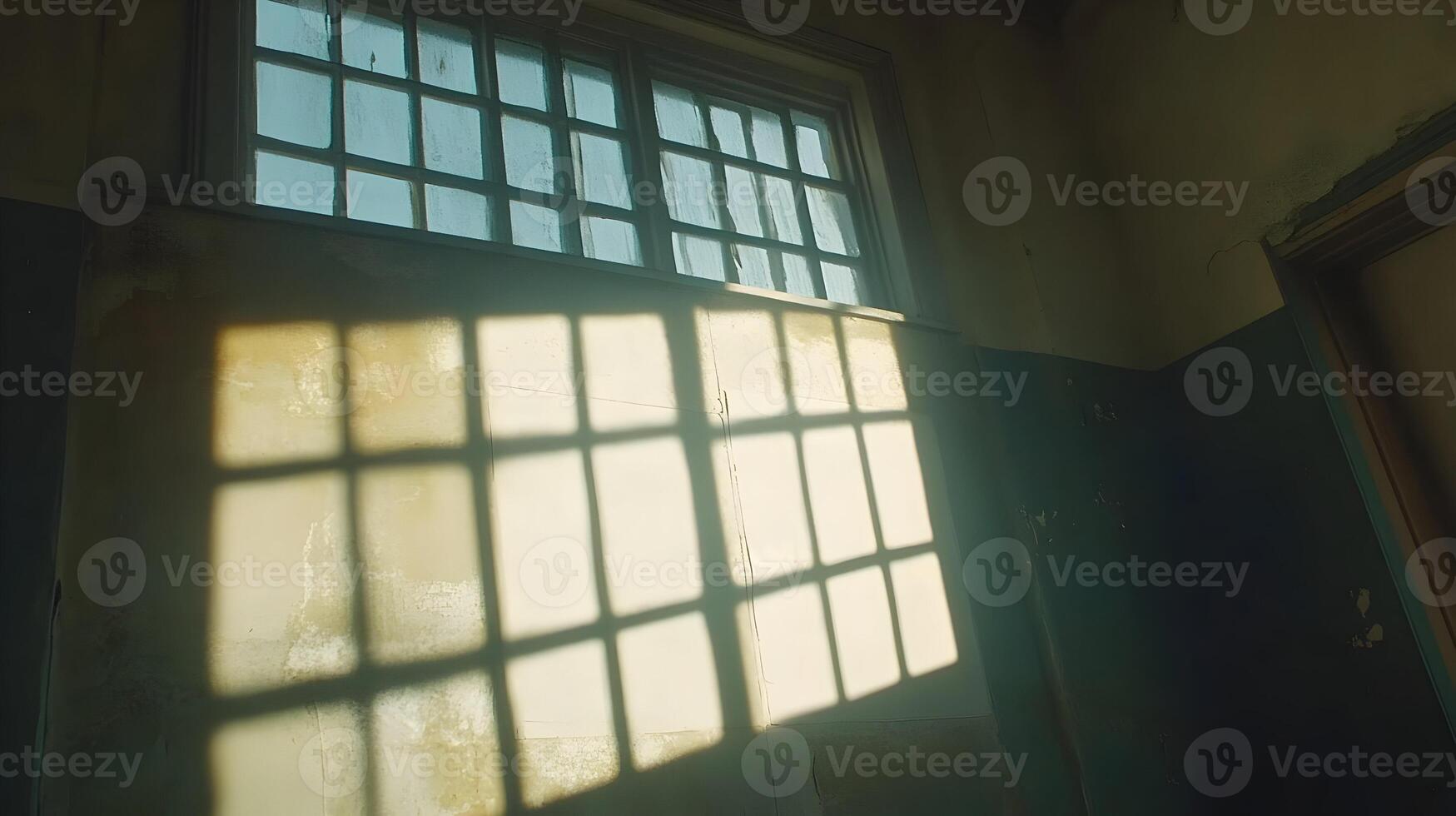 Sunlight streams through a high window in an old, dilapidated building, casting shadows on the wall. photo