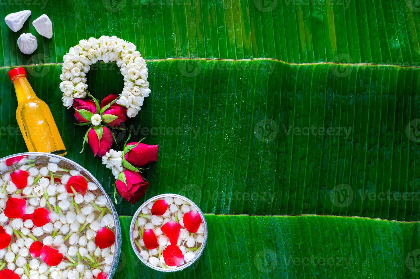 Flowers in water bowl for blessing, scented water and marly limestone with jasmine garland on wet banana leaves background for Thailand Songkran festival background. photo