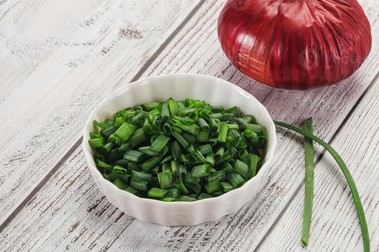 A bowl of chopped green onions and a red onion photo