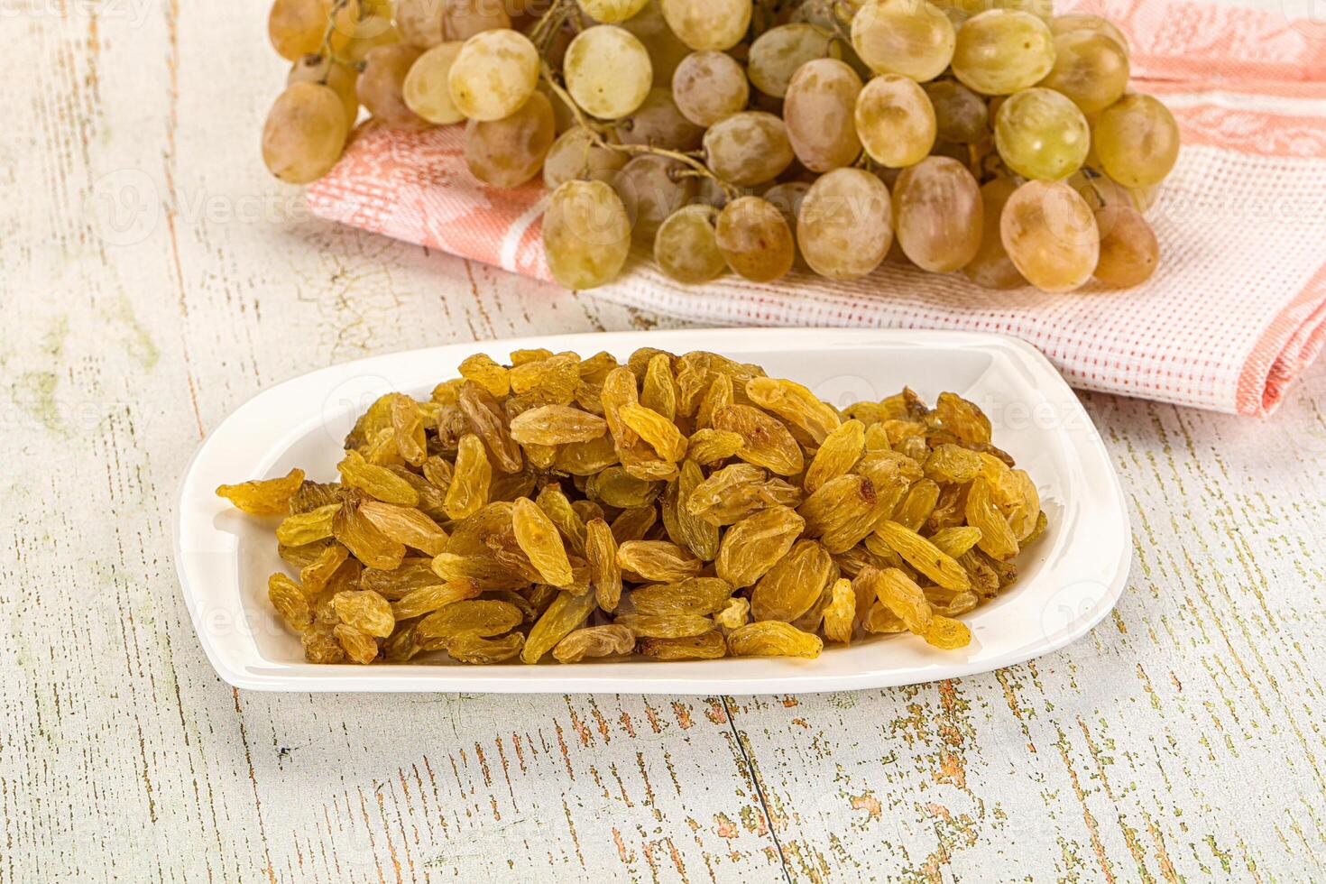 A bowl of raisins and a bunch of grapes on a table photo