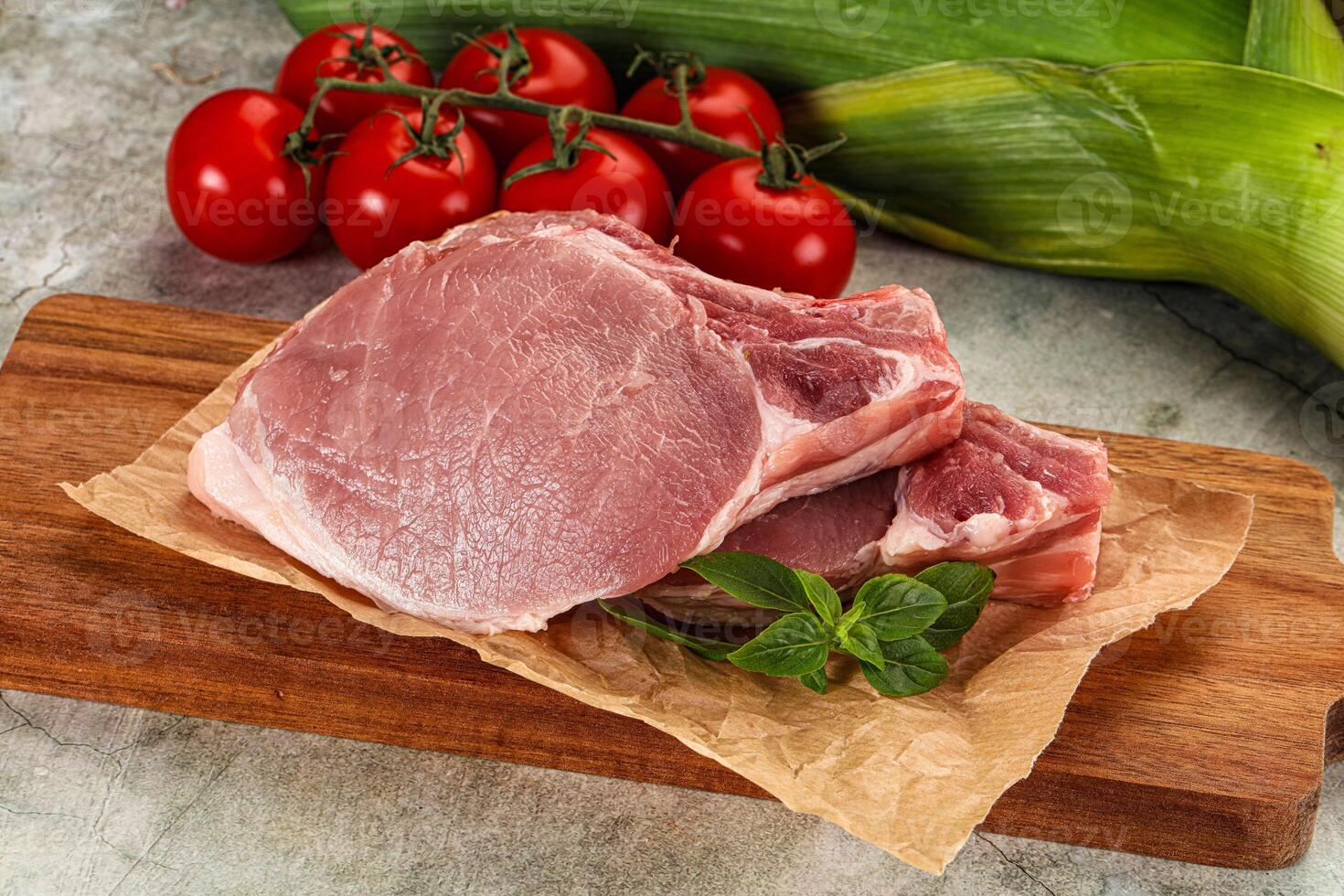 Raw pork on a cutting board with tomatoes and corn photo