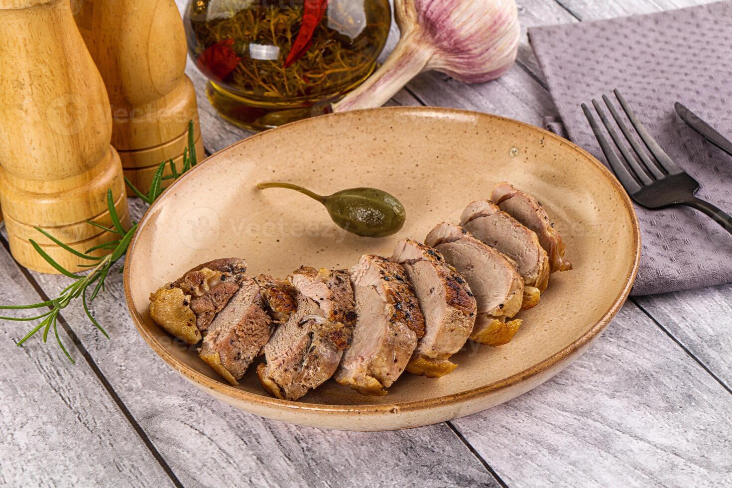 A plate of meat on a wooden table with a knife and fork photo