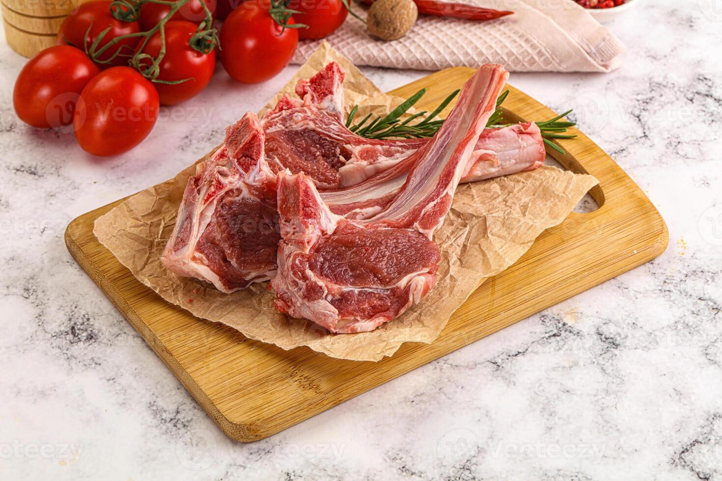 Raw lamb chops on a cutting board with tomatoes and herbs photo
