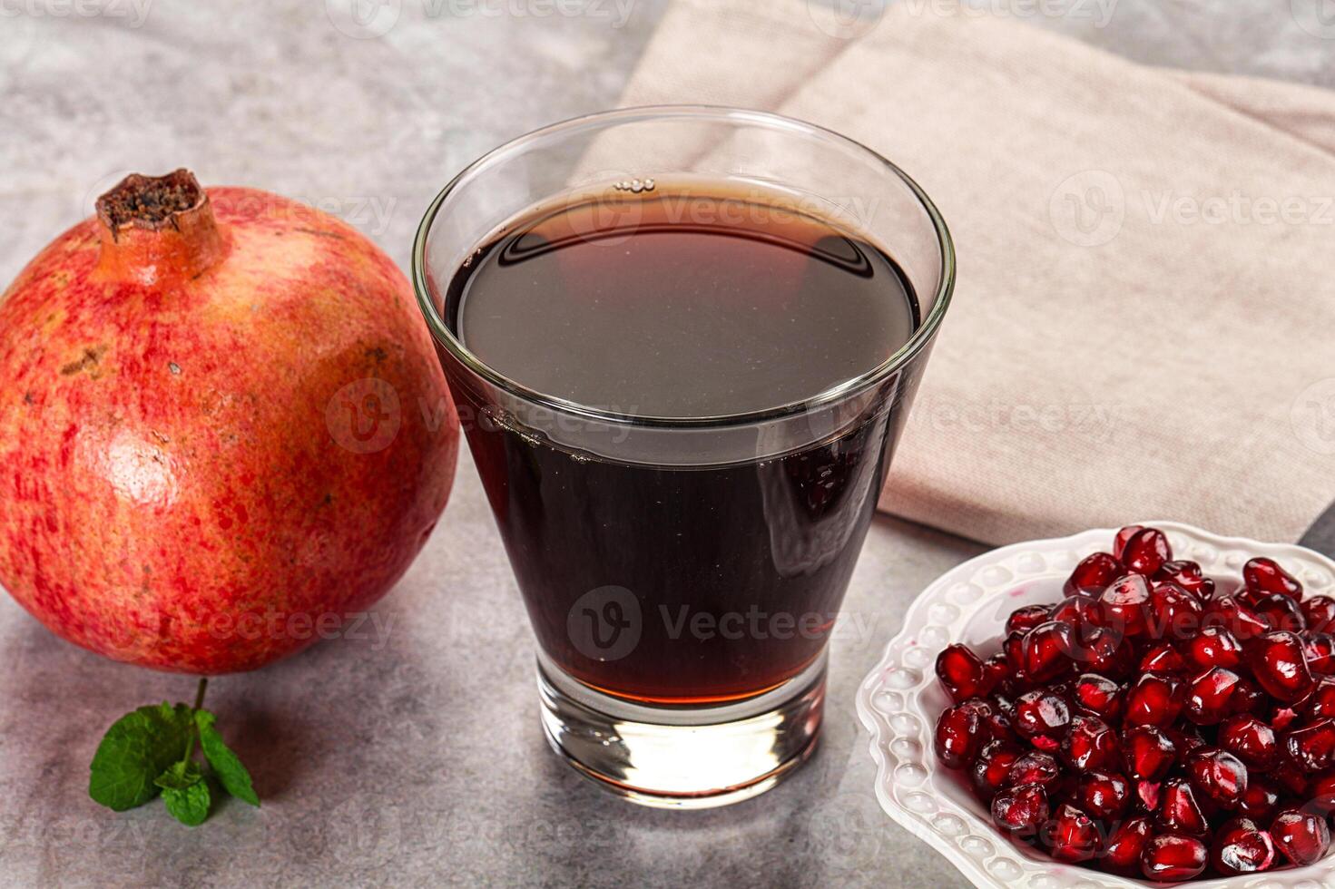 A glass of liquid next to a bowl of pomegranate photo