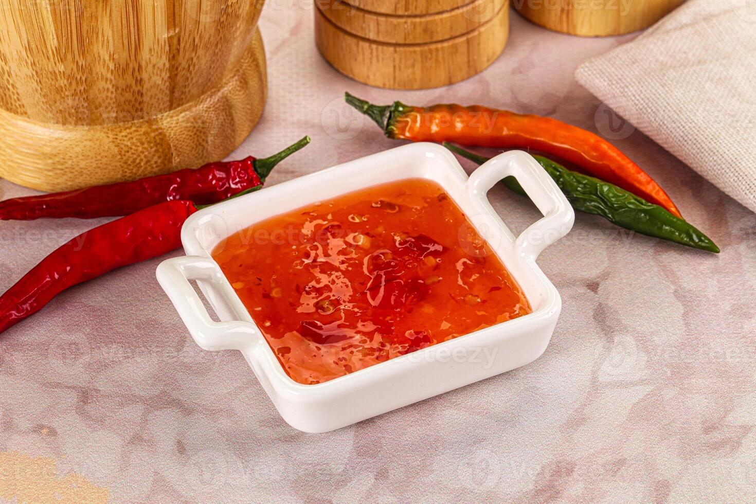 A bowl of chili sauce next to a wooden cutting board photo