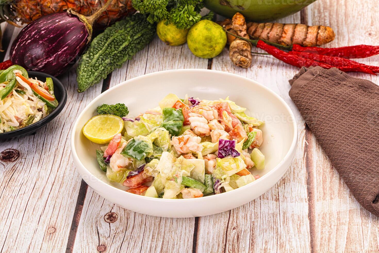 A bowl of salad with vegetables and a napkin on a table photo
