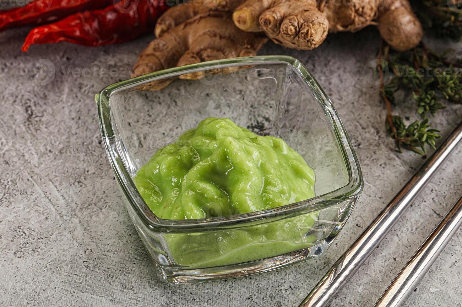 A glass container with a green sauce next to a bowl of ginger and chili peppers photo