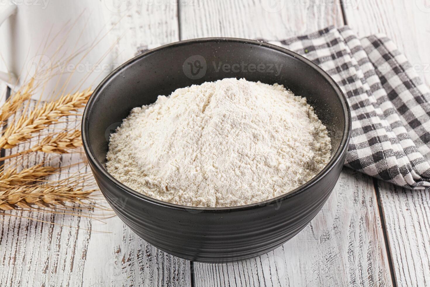 A bowl of flour next to a cup of milk photo