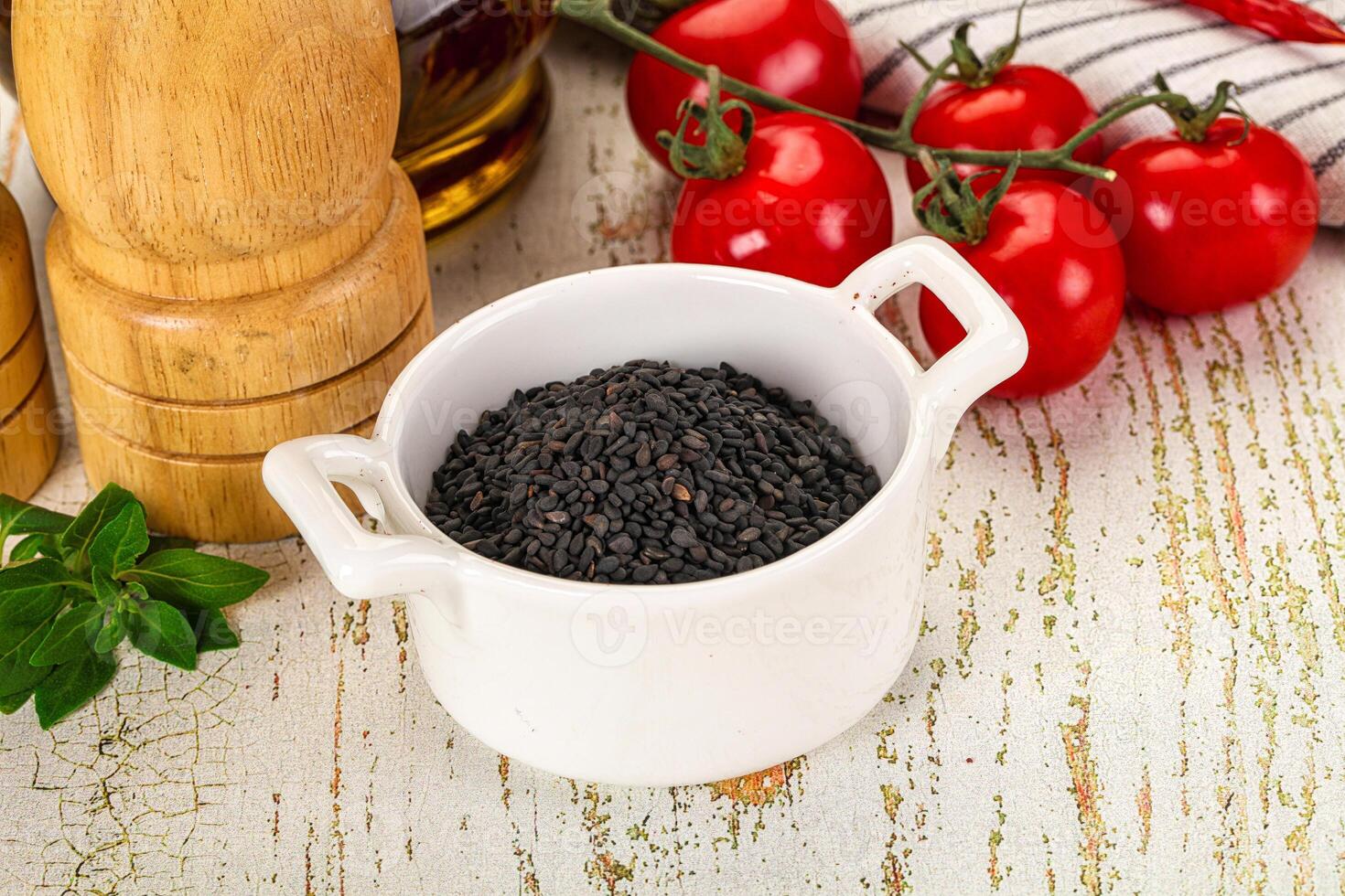 A bowl of black seeds on a table next to a bottle of olive oil photo