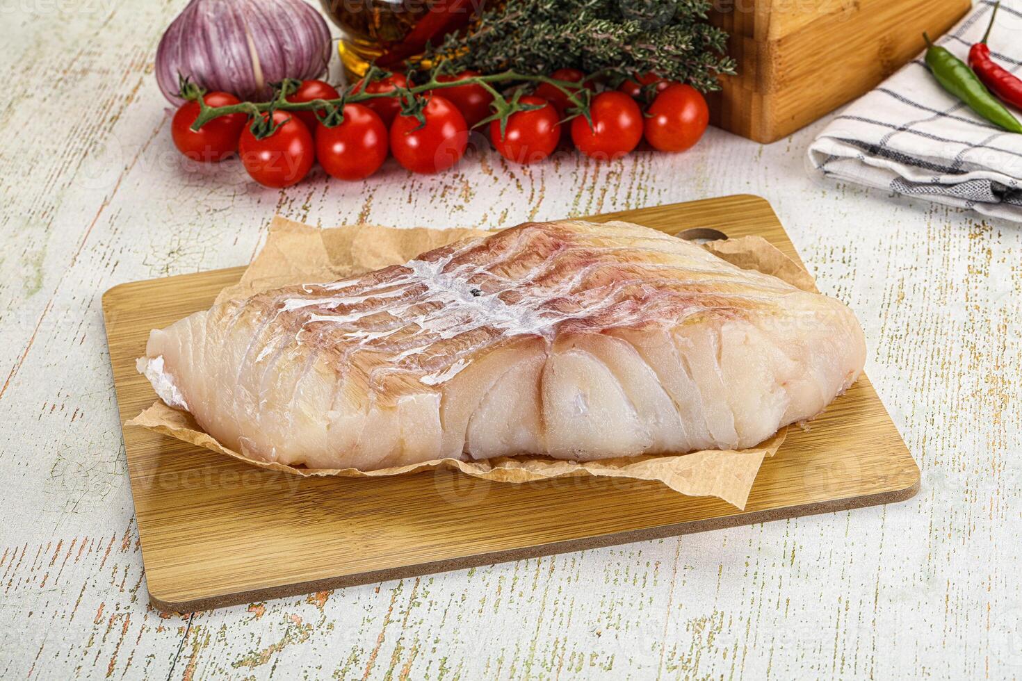 A piece of fish on a cutting board with vegetables and herbs photo