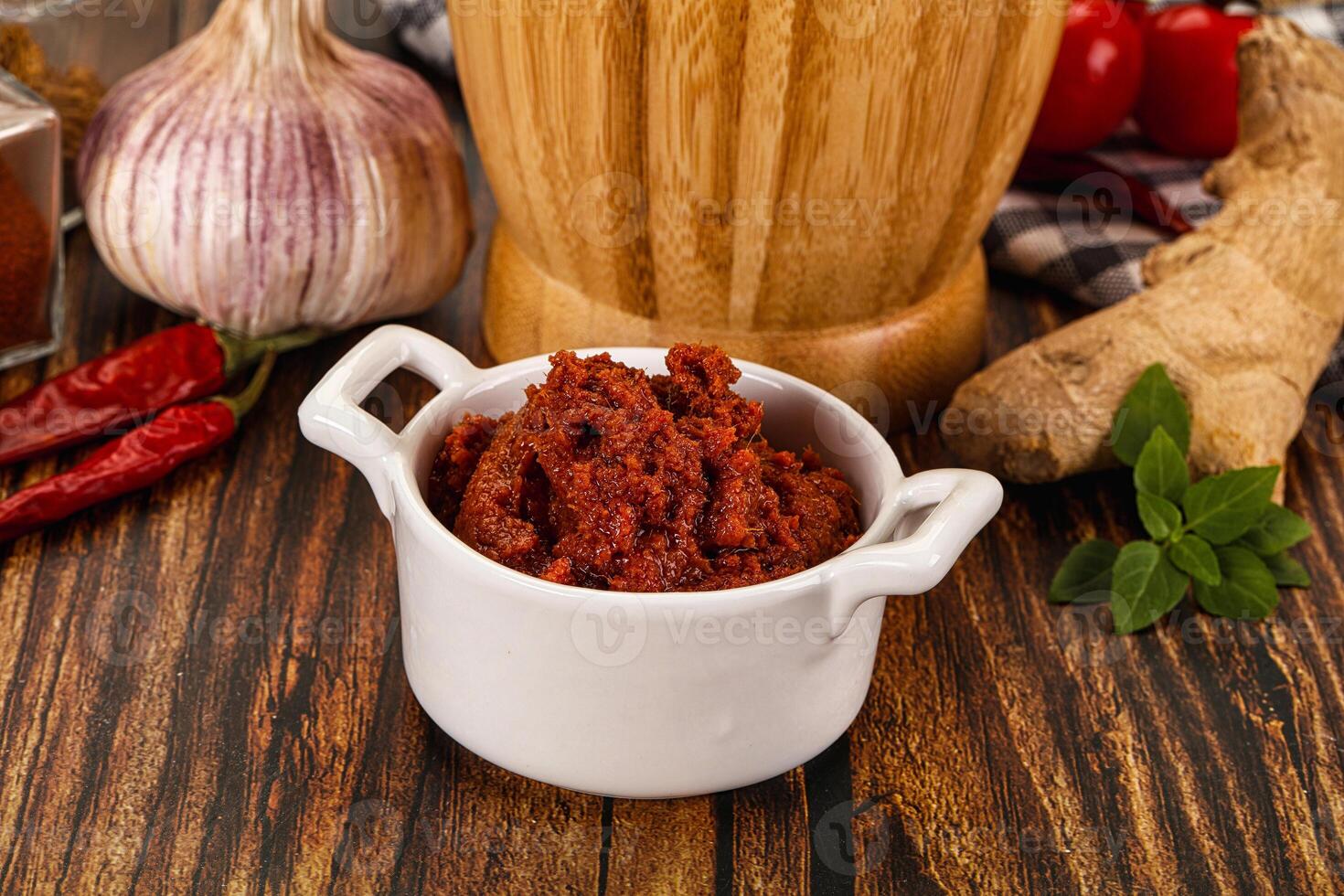 A bowl of chili sauce next to a wooden chopping board photo