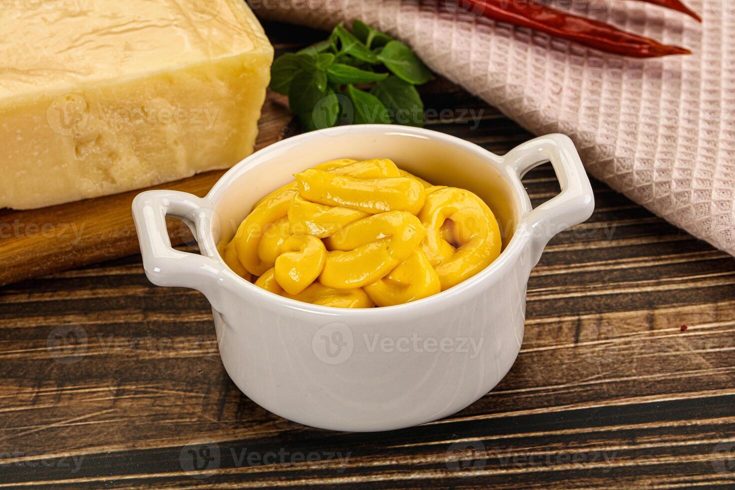 A bowl of macaroni and cheese next to a piece of cheese photo