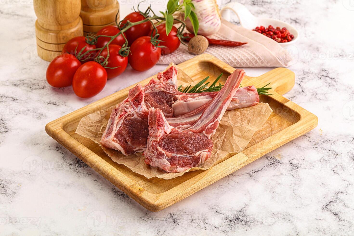 Raw lamb chops on a wooden cutting board with tomatoes and spices photo