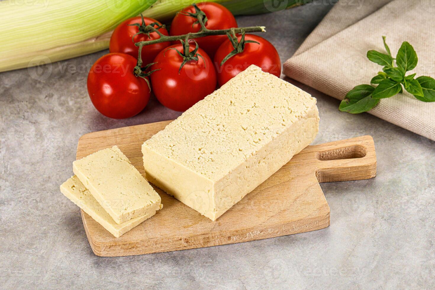 A cutting board with a piece of cheese and tomatoes photo