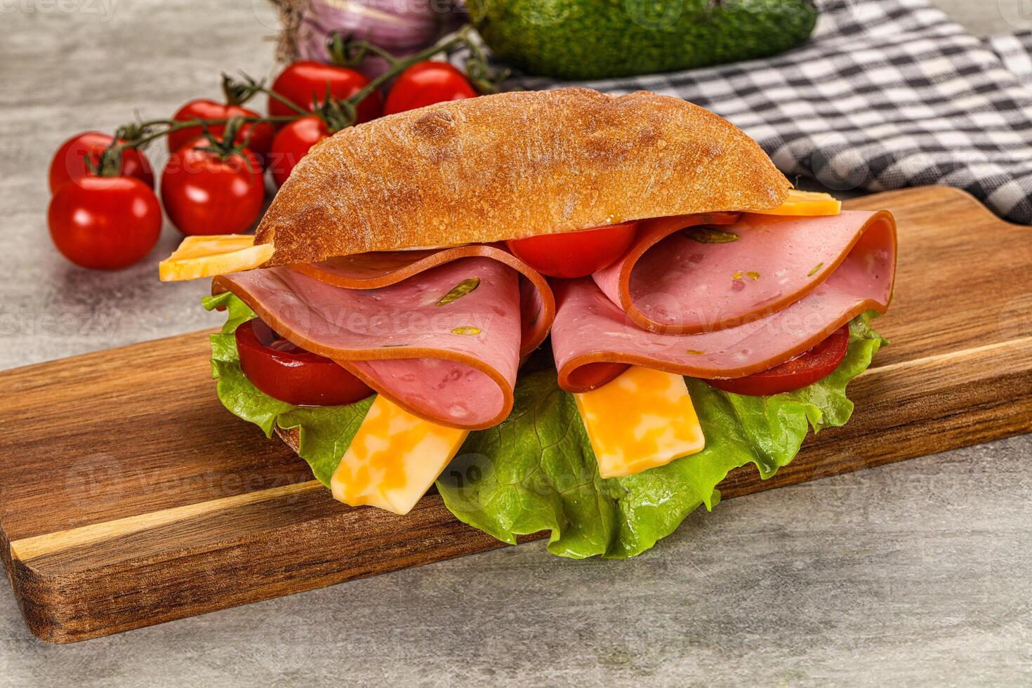 A sandwich with ham, cheese and tomatoes on a wooden cutting board photo