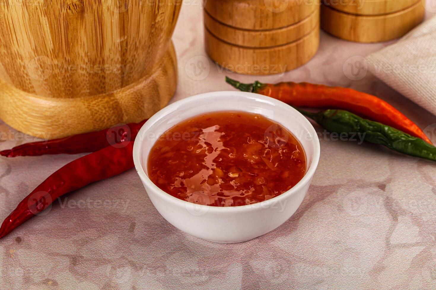 A bowl of chili sauce next to a wooden chopping board photo
