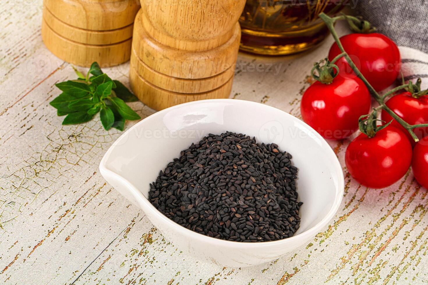 Black sesame seeds in a bowl next to tomatoes and spices photo