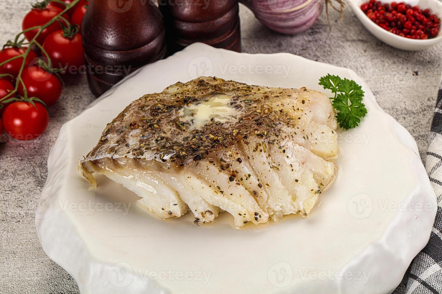 A piece of fish on a white plate with herbs and tomatoes photo