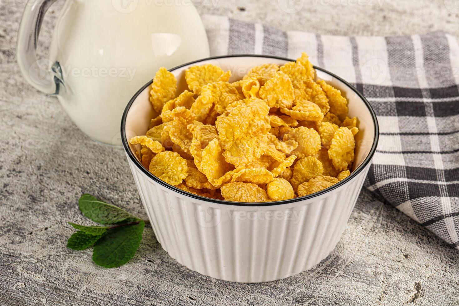 Corn flakes in a white bowl with milk and a green leaf photo