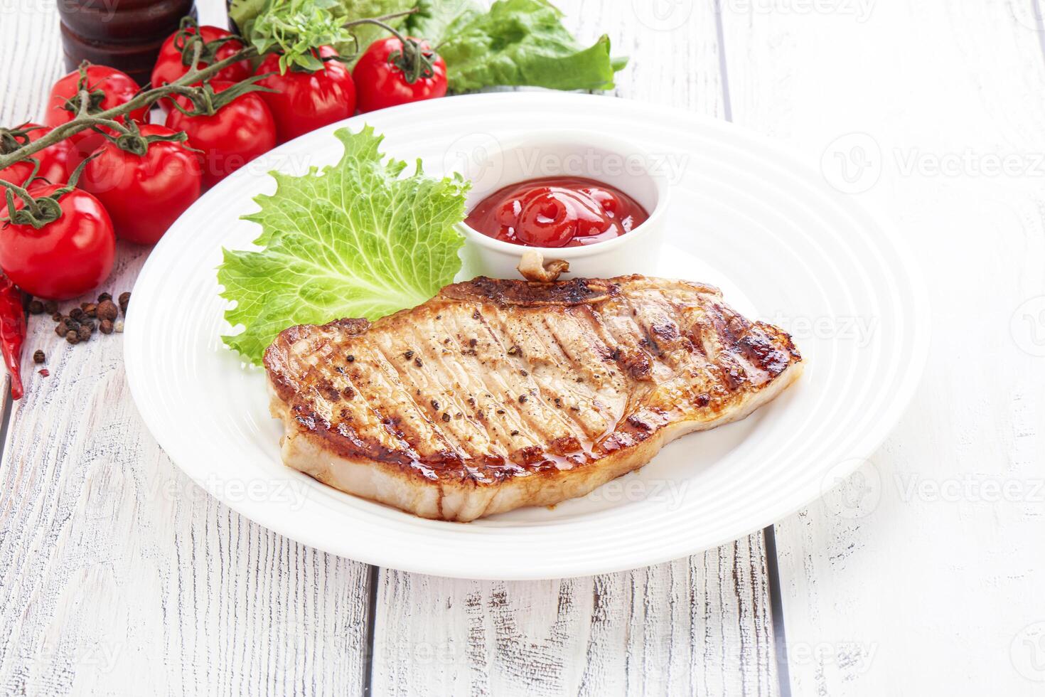 Grilled pork steak with tomato sauce and lettuce on a white plate photo