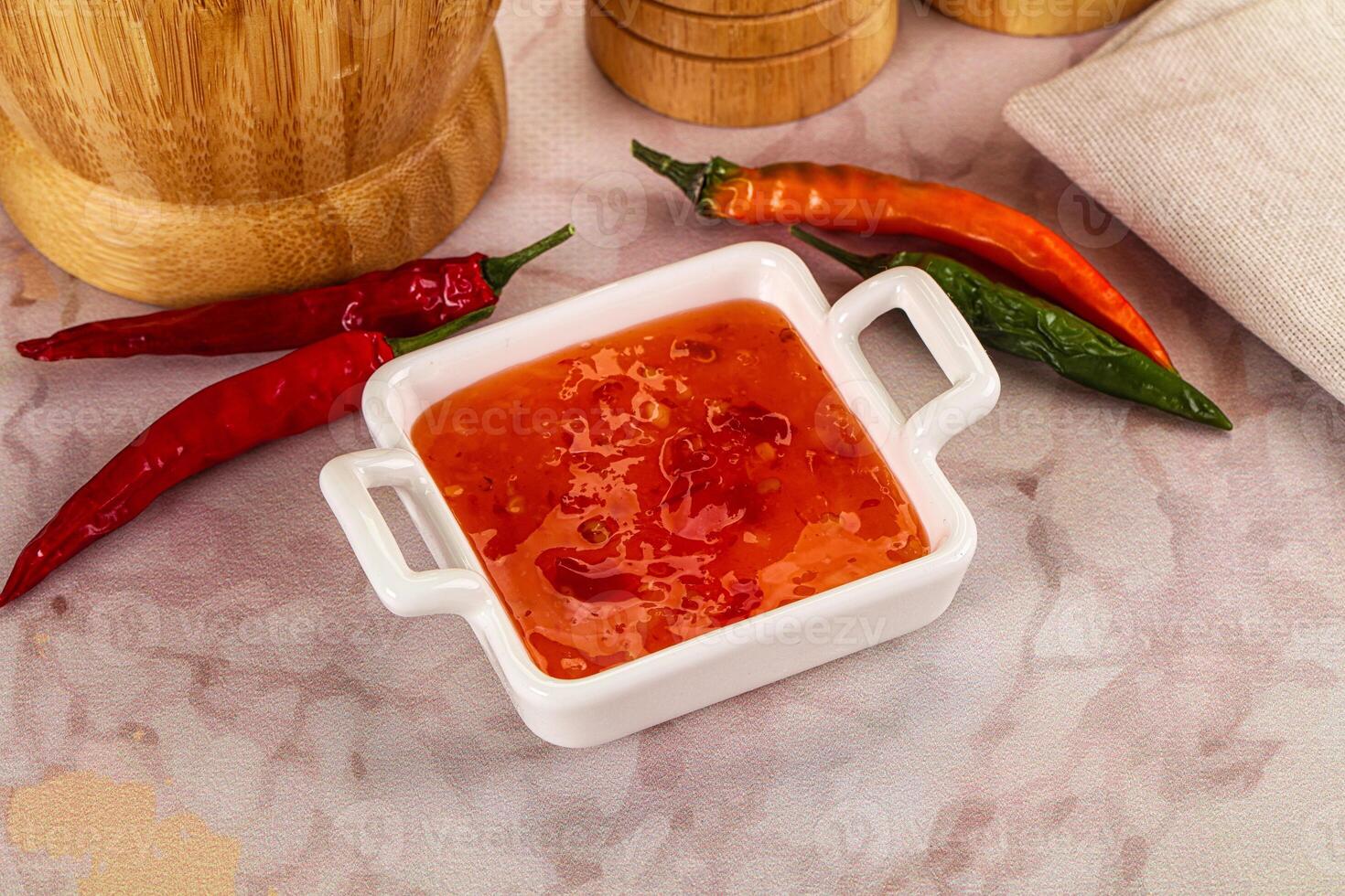A bowl of chili sauce next to a wooden chopping board photo